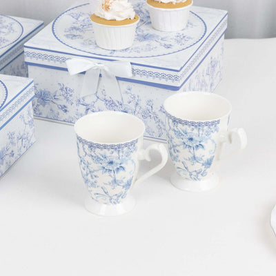 Blue floral porcelain mugs with heart-shaped handles on a white table.