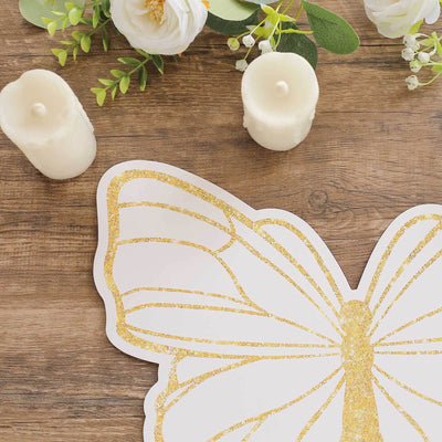 Gold glitter butterfly decoration on wooden table with candles and flowers.