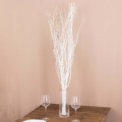 White decorative branches in a glass vase on a wooden table.