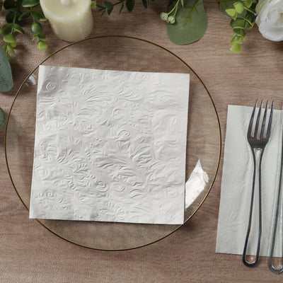 Textured white napkin on a decorative plate with cutlery and floral accents.