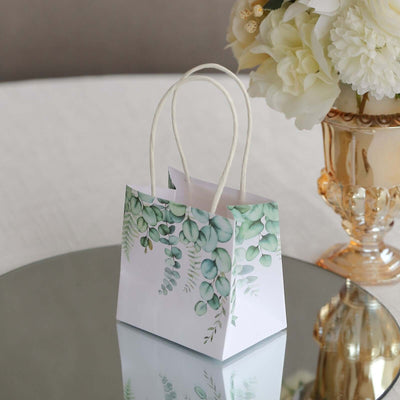 Decorative gift bag with green foliage design on a mirrored surface.