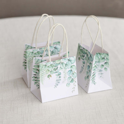 Decorative gift bags with green foliage design on a neutral background.