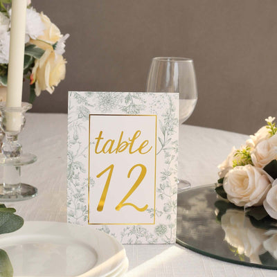 Table number sign with floral design and gold accents on a dining table setting.