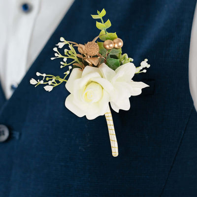 White rose boutonniere with greenery and decorative accents on a suit jacket.