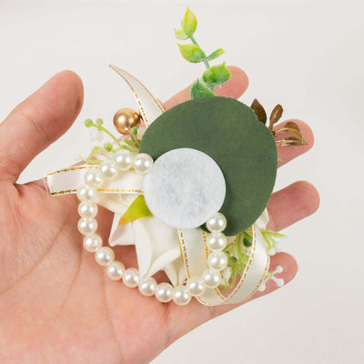 Floral boutonniere with pearls and greenery in hand.