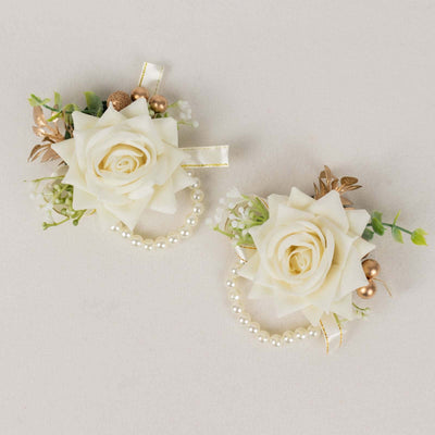 White rose corsages with pearls and gold accents on a neutral background.