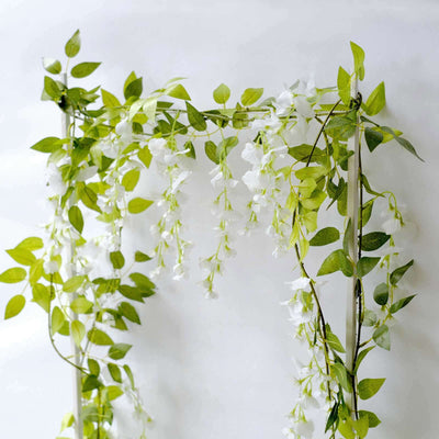 Artificial white floral vine with green leaves on a plain backdrop.