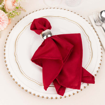 Red napkin elegantly arranged on a decorative plate with a silver napkin ring.