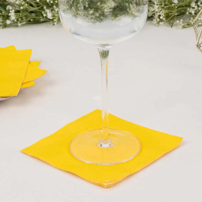 Yellow cocktail napkin under a glass on a table.
