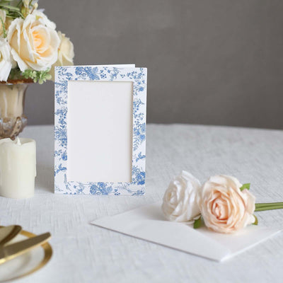 Floral-patterned photo frame with blank space and envelope on a table.
