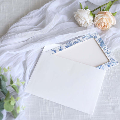 White envelope with floral border and blank insert on soft fabric background.