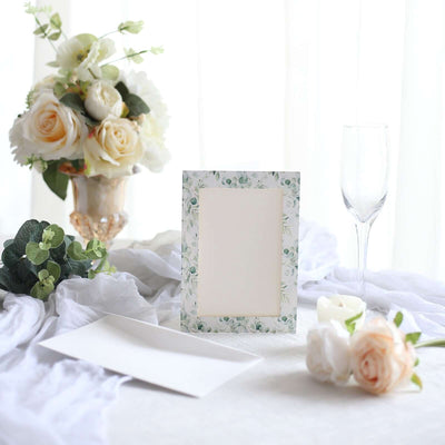 Floral picture frame on a table with roses and glassware.
