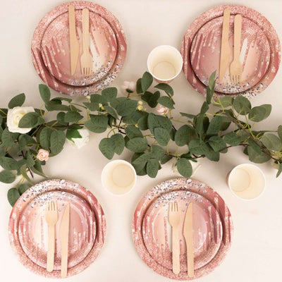 Elegant pink disposable plates with wooden cutlery and greenery for a stylish table setting.