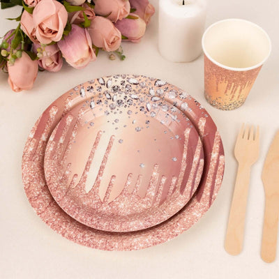 Pink glitter party plates and cup with wooden utensils against a floral backdrop.