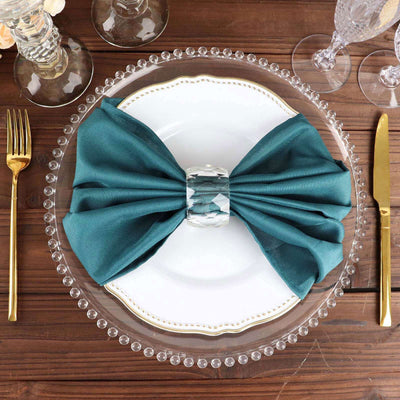 Elegant teal napkin bow on a white plate with crystal napkin ring and gold cutlery.