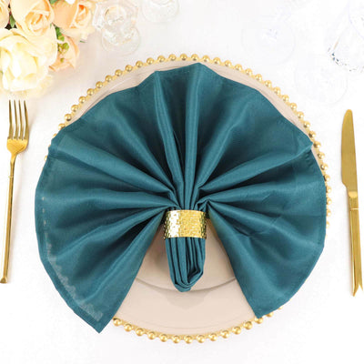 Teal napkin elegantly folded on a gold-rimmed plate with floral arrangement.