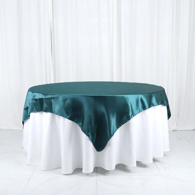 Teal satin tablecloth draped over a round table with a white undercloth.