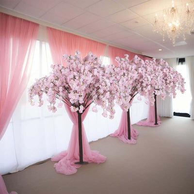 Pink cherry blossom trees with draped fabric in a decorated indoor setting.