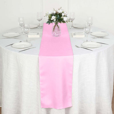 Pink table runner on a dining table set with glassware and plates.