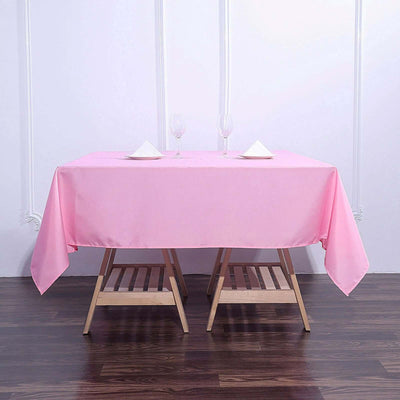 Pink tablecloth on a wooden table set for dining with glasses and napkins.