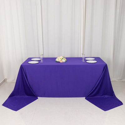 Purple tablecloth with white plates and floral centerpiece on a plain backdrop.
