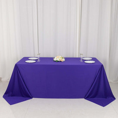 Purple banquet table with white plates and floral centerpiece.