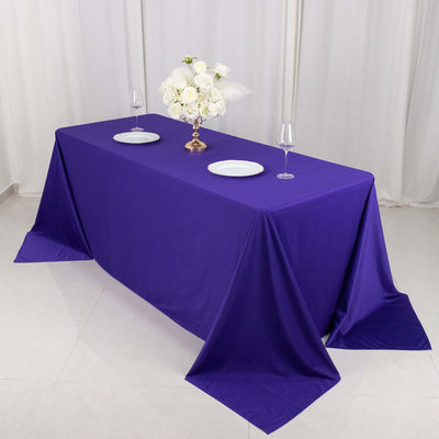 Purple tablecloth draped over a table with plates and a floral centerpiece.