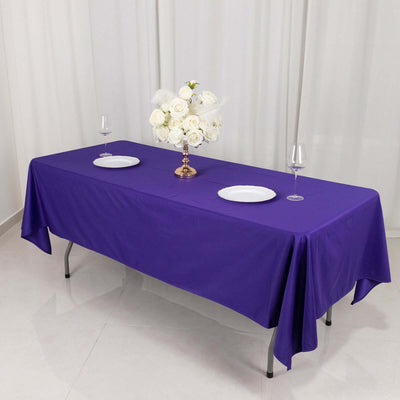 Purple tablecloth draped over a table with plates and a floral centerpiece.