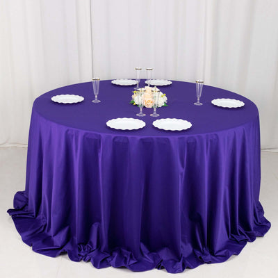 Purple round tablecloth draped over a table with white plates and floral centerpiece.