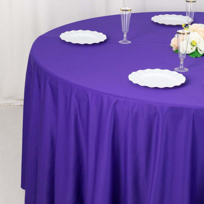 Purple tablecloth draped over a round table with white plates and floral centerpiece.