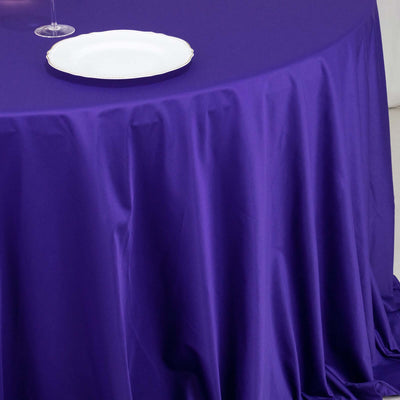 Purple tablecloth draping over a round table with a white plate on top.
