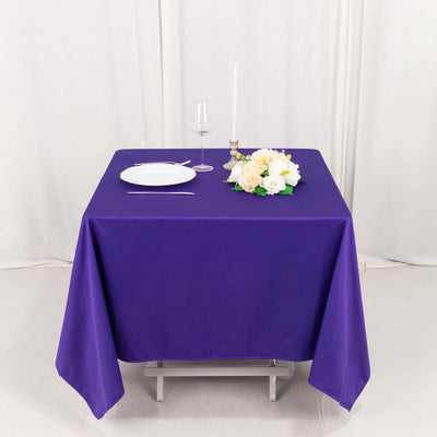 Purple tablecloth draped over a table set with a plate, glass, and floral centerpiece.