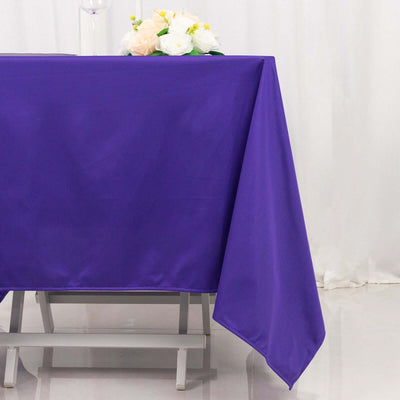 Purple tablecloth draped on a table with flowers in the background.