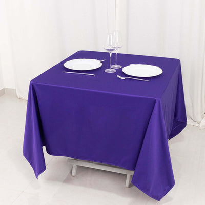 Purple tablecloth draped over a table with plates and glasses set on top.