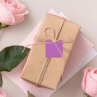 Gift box wrapped in brown paper with a purple tag and surrounded by pink roses.