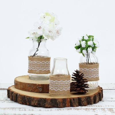 Decorative glass vases with burlap accents and faux flowers on a wooden slice.