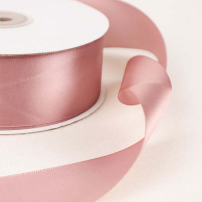 Pink satin ribbon roll with flowing end on a plain background.
