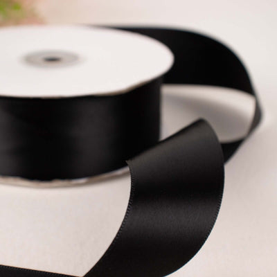 Black satin ribbon roll with a smooth finish and loose end.