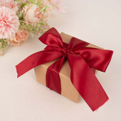 Brown gift box with a red satin ribbon and floral background.