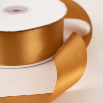 Gold satin ribbon roll with a flowing end on a soft background.