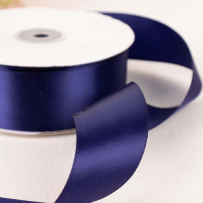 Navy blue satin ribbon on a spool with a flowing end.