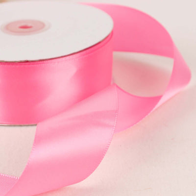 Pink satin ribbon on a spool with loose ribbon draped