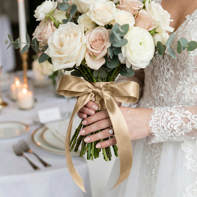 Bride holding ivory rose wedding bouquet with gold ribbon and eucalyptus