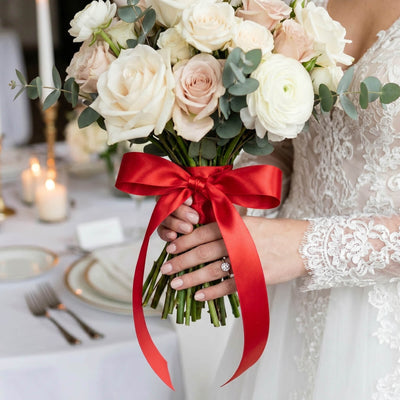 Bride holding white and blush rose bouquet with red ribbon at wedding reception