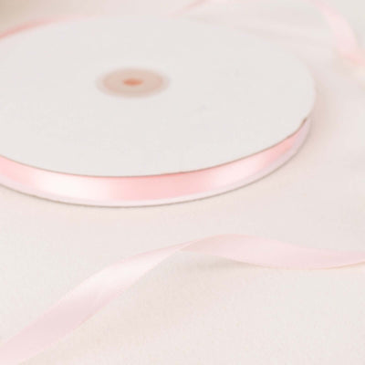 Pink satin ribbon roll with loose ribbon strand on white background.