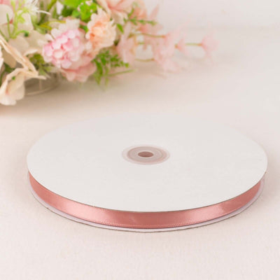 Rose gold satin ribbon on a spool with floral backdrop.