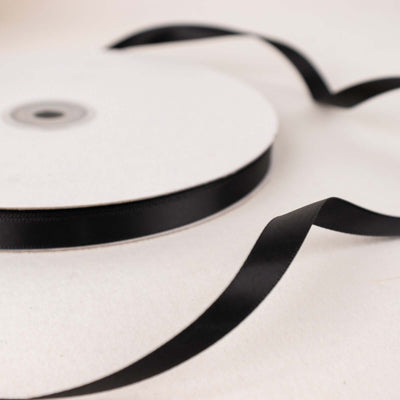 Black satin ribbon on a spool with loose ends displayed.