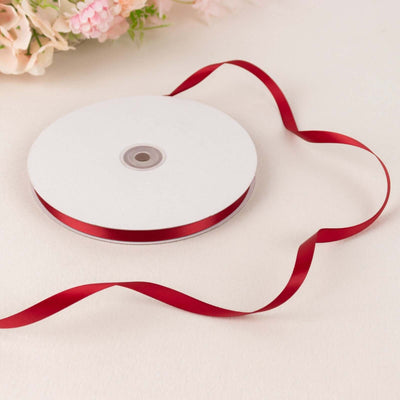 Red satin ribbon on a spool with a flowing ribbon end.