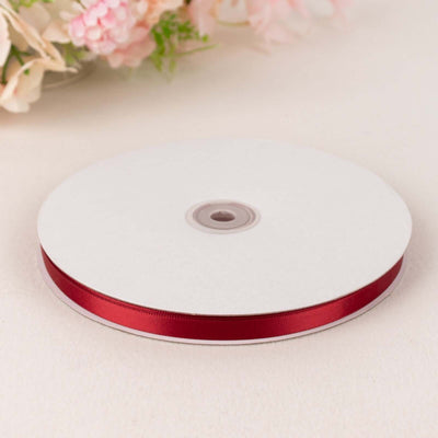 Red satin ribbon on a spool, perfect for crafts and decorations.