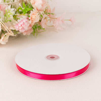 Pink satin ribbon on a spool with floral background.